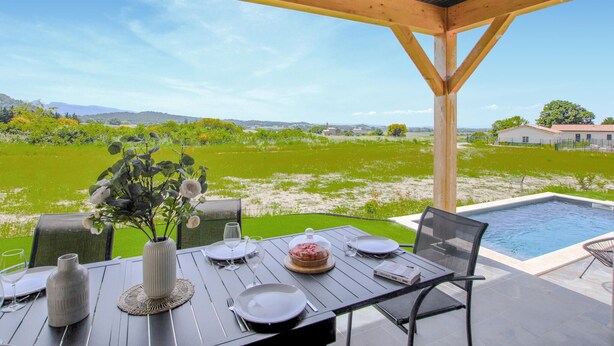 An outdoor dining area with a view of a green field and a swimming pool. - Lovely home in Puy St Martin (Puy St Martin)