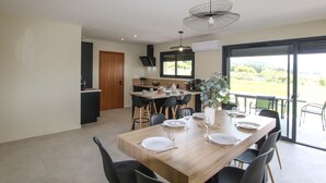 A modern dining area with a wooden table set for four, black chairs, and a view of a garden through a large sliding glass door. - Lovely home in Puy St Martin (Puy St Martin)