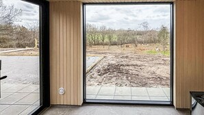 Een kamer met een grote schuifpui die uitkomt op een buitenruimte met een grond van aarde en bomen.