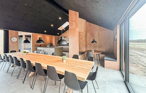 A modern kitchen with a central island, black pendant lights, and a dining area with a long wooden table and chairs.