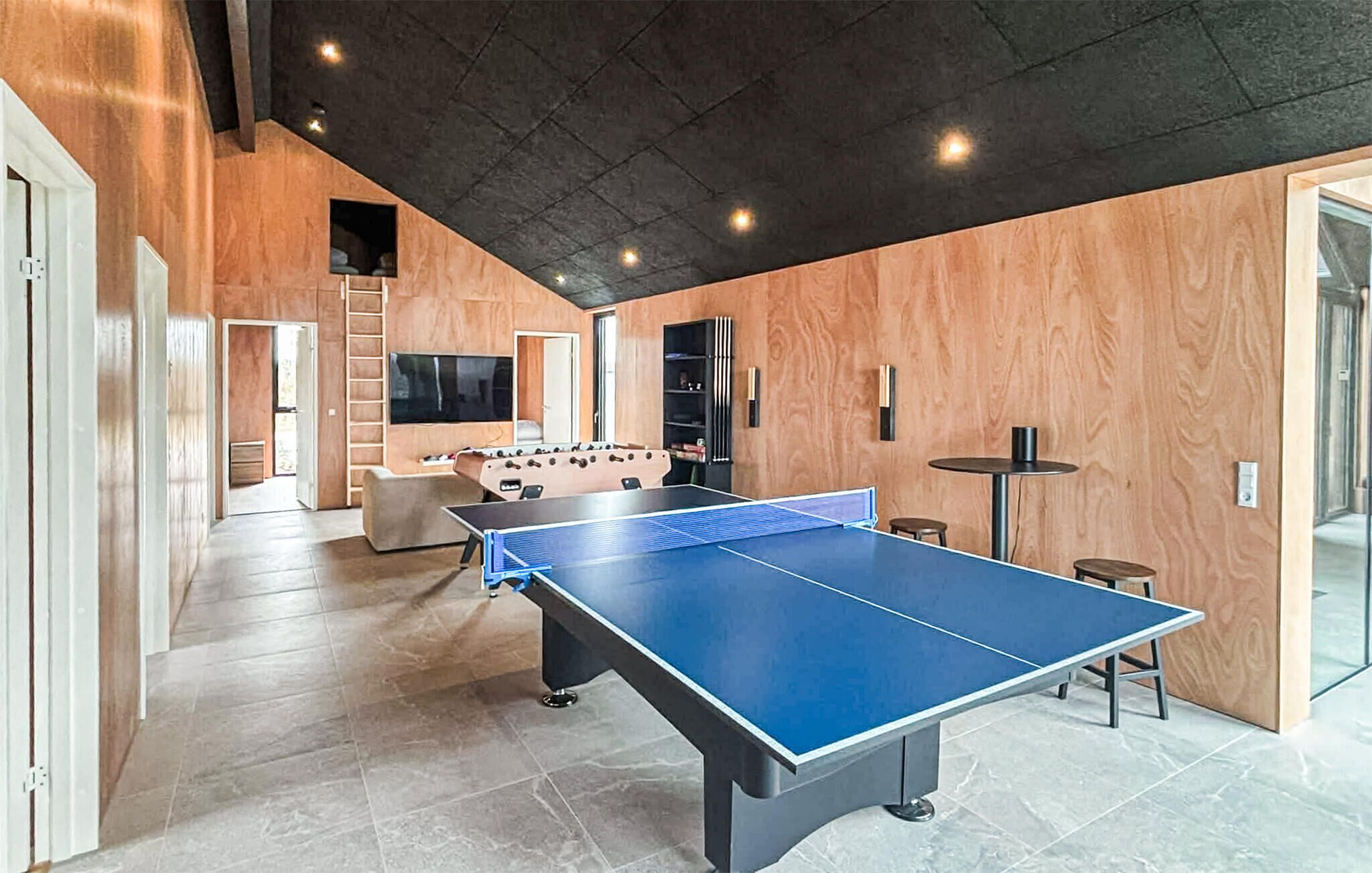 Una habitación amplia con mesa de ping pong, mesa de futbolín y televisor montado en la pared.