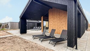 Een modern gebouw met een schuin dak, een terras met loungestoelen en een houten wand.