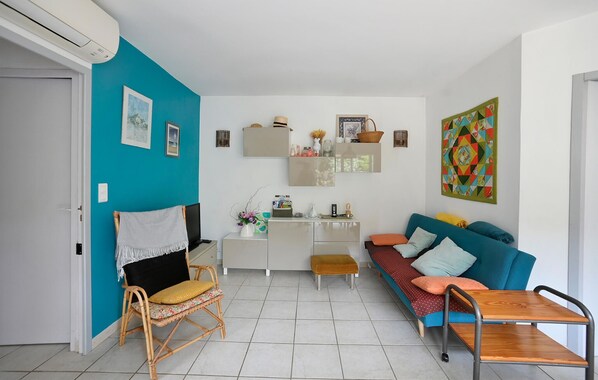 A living room with a teal wall, a blue sofa, a wooden coffee table, a wicker chair, and a small wooden stool. - Nice home in Serignan-du-comtat (Serignan-du-comtat)