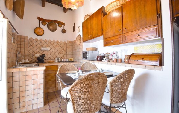 A kitchen with wooden cabinets, a tiled backsplash, and a dining area with wicker chairs.