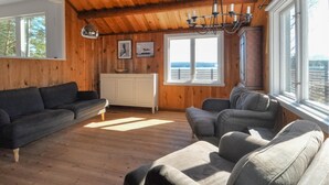 Een gezellige woonkamer met houten wanden en vloeren, een witte kast en een groot raam met uitzicht op het water.