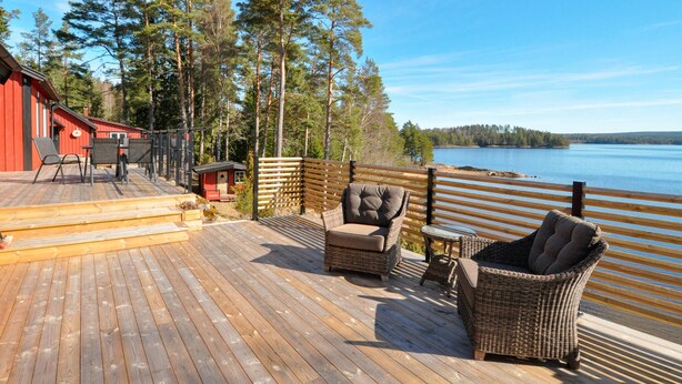 Een houten terras met rieten meubilair, een rood gebouw en uitzicht op een meer.