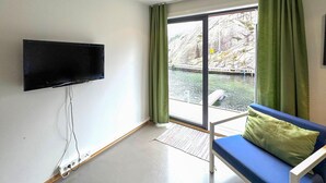 A room with a TV mounted on the wall, a blue sofa with a green pillow, and a view of a river and bridge outside. - Pet friendly apartment in Søgne (Søgne)