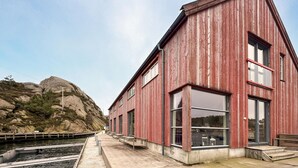 A red wooden building with large windows, a concrete platform, and a rocky hill in the background. - Pet friendly apartment in Søgne (Søgne)