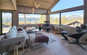 Un interior moderno con ventanas amplias, un sofá, una silla y una mesita con un jarrón de flores.