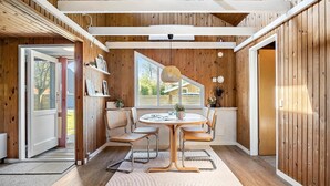 A cozy room with a wooden interior, a round table with chairs, a large window, and a door leading outside.