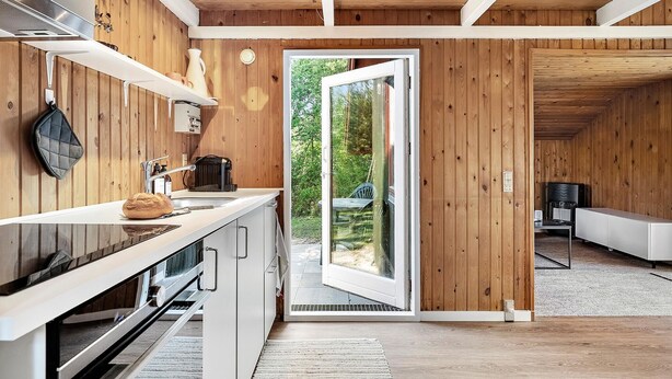 A modern kitchen with wooden walls, a built-in oven, and a large window opening to a patio.