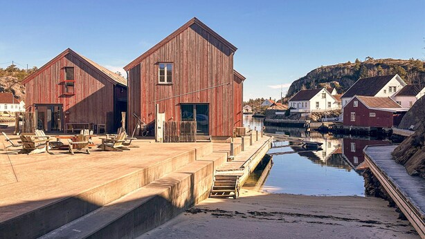 A waterfront property with two wooden buildings, a dock, and a calm water body reflecting the structures.