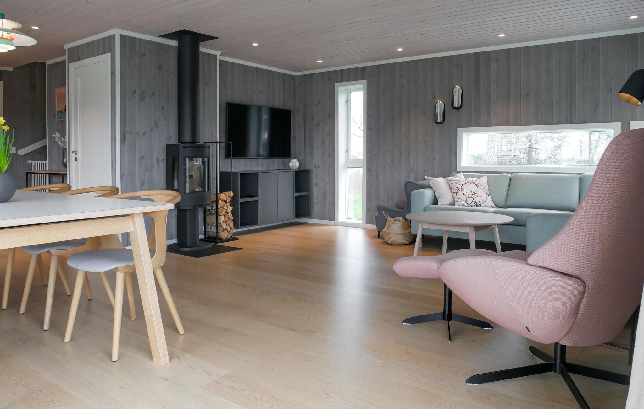 A modern living room with a fireplace, a dining area with wooden furniture, and a sofa with a view of the outdoors.