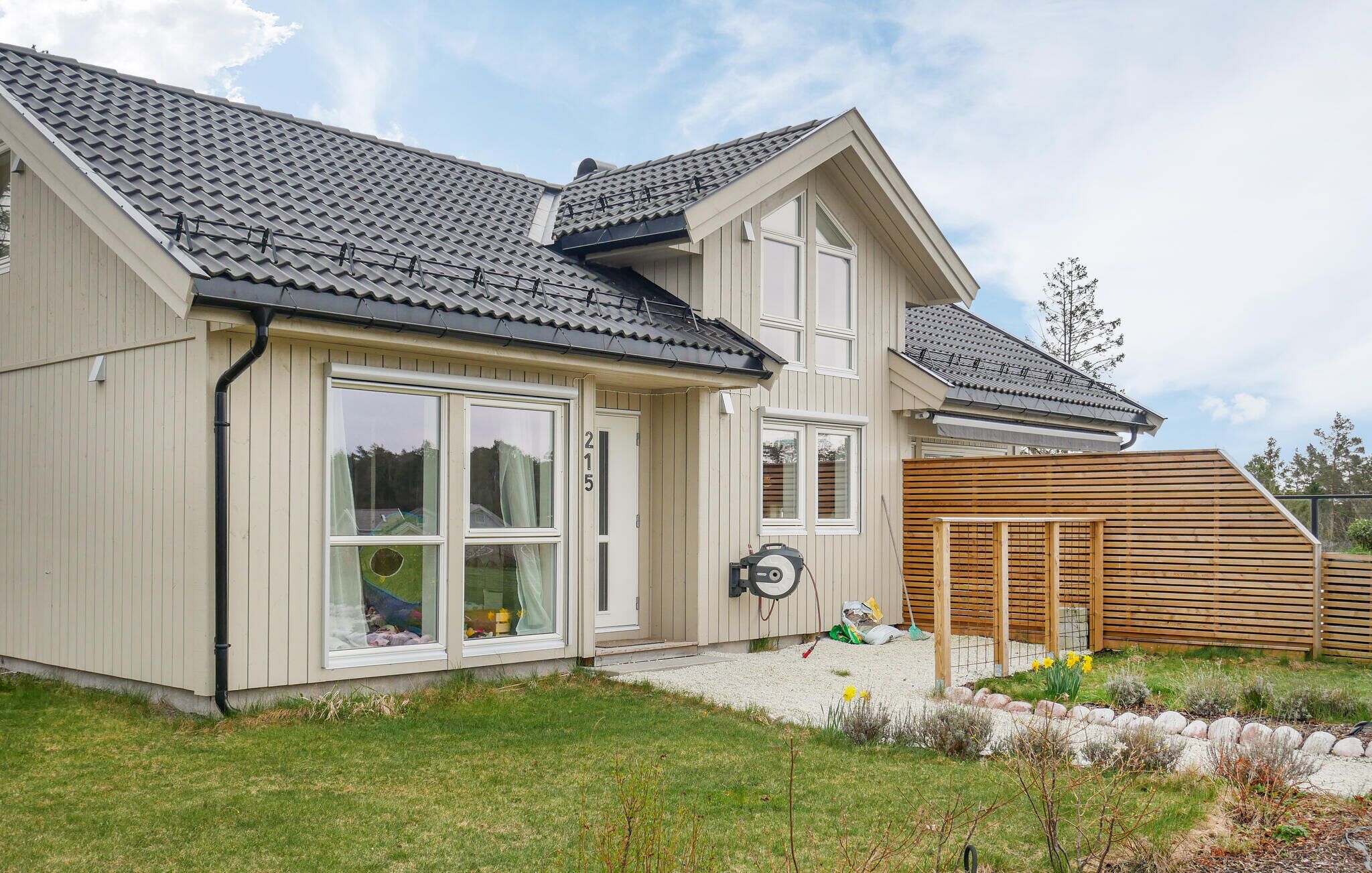 Une maison à deux étages avec un toit recouvert de tuiles grises, de grandes fenêtres et une clôture en bois.