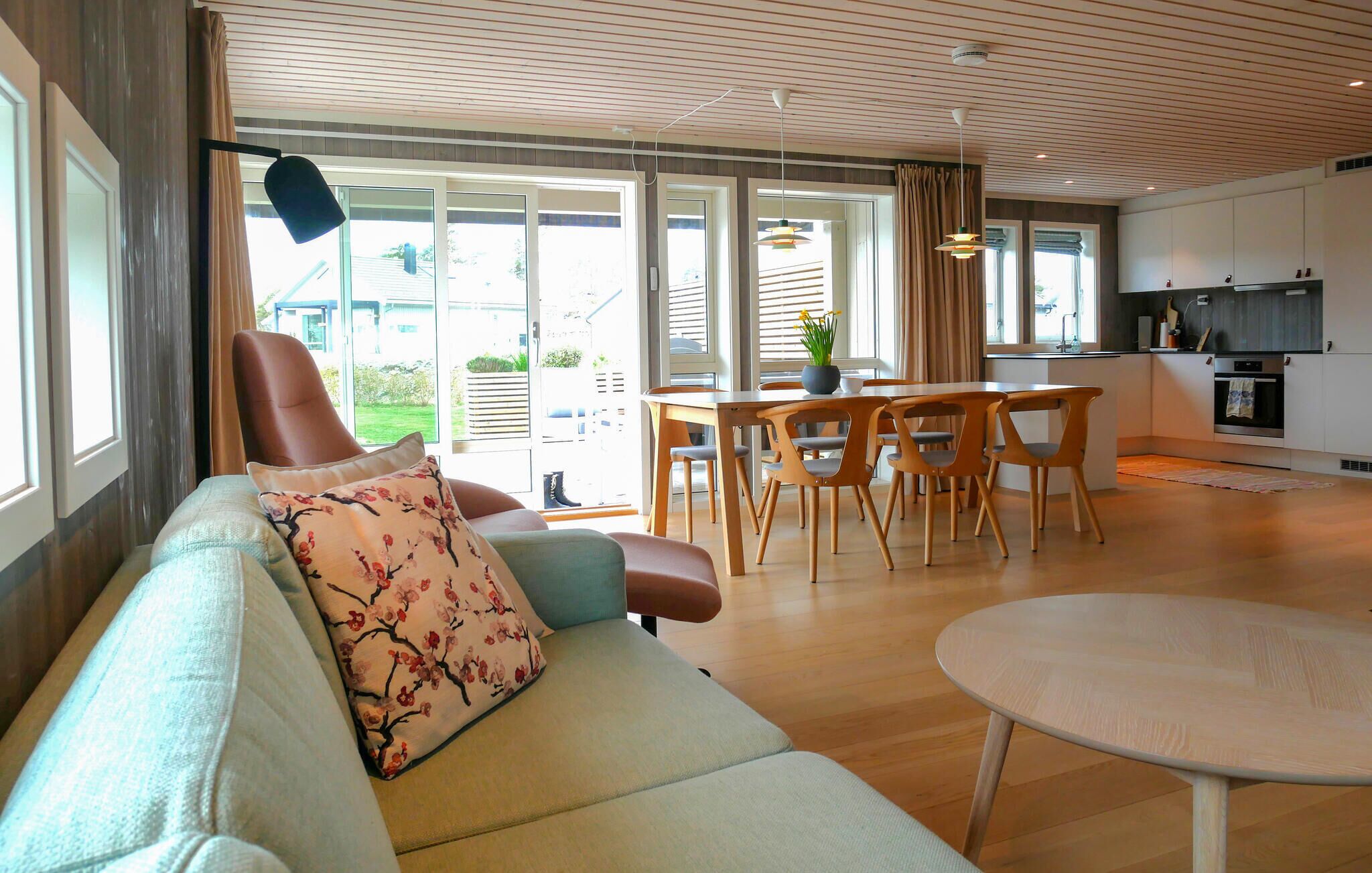 En moderne stue med sofa, spisebord med stole og et køkken med komfur og skabe.