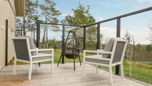 A covered outdoor area with two white chairs and a hanging chair, overlooking a grassy landscape with trees. - 4 bedroom cozy home in Færvik (Færvik)