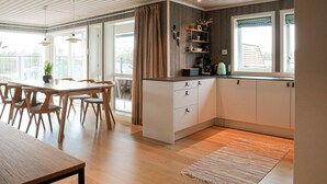 A modern kitchen with white cabinets, a wooden dining table, and a large window. - 4 bedroom cozy home in Færvik (Færvik)