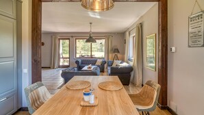 A spacious dining area with a wooden table and chairs, a hanging light fixture, and a view of the garden through large windows. - Beautiful home in Olsztynek (Olsztynek)