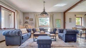 A spacious living room with a large sofa set, a coffee table, and a pendant light. There are windows with curtains, a map on the wall, and a kitchen area visible in the background. - Beautiful home in Olsztynek (Olsztynek)