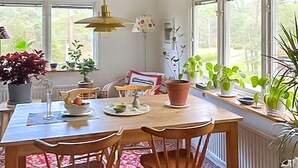 Un coin repas avec une table en bois, deux chaises, une plante en pot et une fenêtre donnant sur un paysage verdoyant.