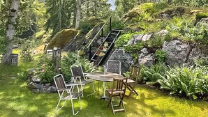 Un espace repas avec une table ronde et des chaises, entouré d’une végétation luxuriante et adossé à un paysage rocheux.