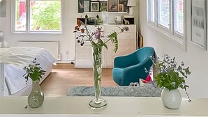 Une chambre à coucher avec un lit, une commode, une chaise et un vase rempli de fleurs.