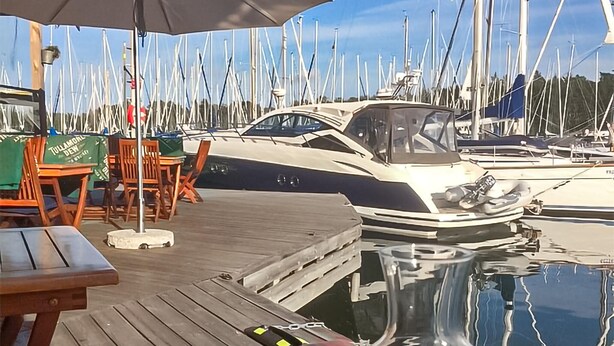 Un port de plaisance avec des bateaux amarrés, des chaises en bois, une table et un parasol.