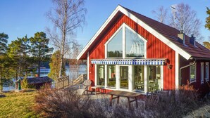 Una cabaña de madera roja con un amplio ventanal y ventanas, un porche con sillas y vistas a un lago.