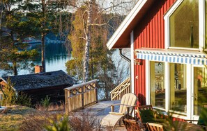 A wooden deck with chairs, a glass door, and a view of a lake. - Amazing home in Väto with sauna (Väto)