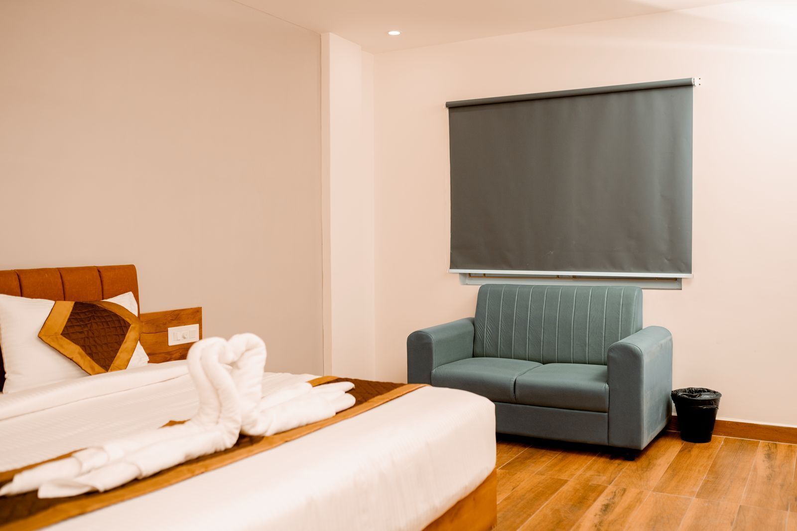 Une chambre d’hôtel avec un lit, un canapé, une fenêtre avec un store et une poubelle.