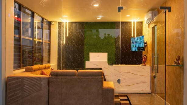 A modern living room with a sofa, a glass partition, a green wall, and a television. - Hotel Elite Fortune Inn (Tirupati)
