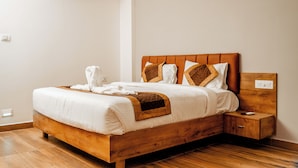 A wooden bed with white bedding, a nightstand, and a small drawer. - Hotel Elite Fortune Inn (Tirupati)