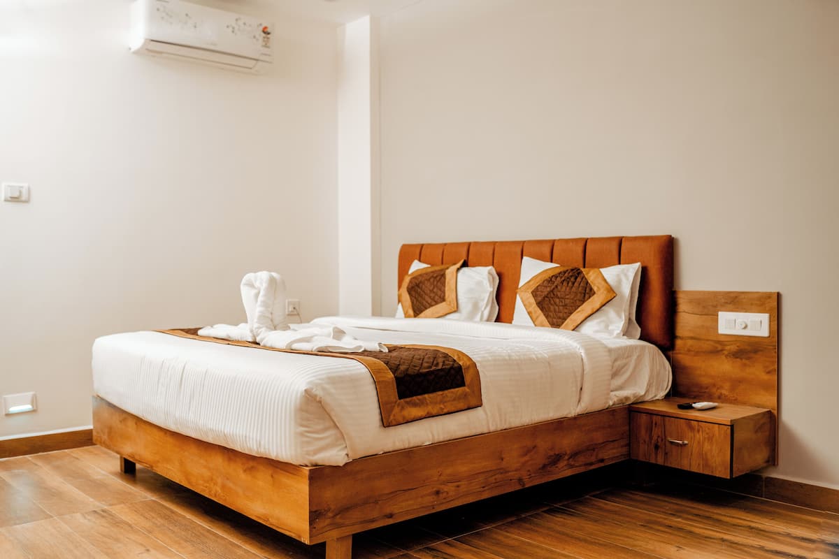 A wooden bed with white bedding, a nightstand, and a small drawer.