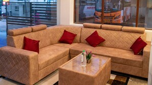 A beige sectional sofa with red cushions, a glass coffee table, and a view of a bus through a window. - Hotel Elite Fortune Inn (Tirupati)