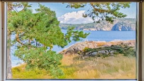 A window with a view of a coastal landscape, including trees, grass, and a rocky shoreline. - Beautiful home in Lysekil (Lysekil)