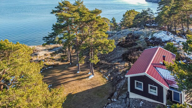 A cabin with a red roof overlooking a lake, surrounded by trees and rocky terrain. - Beautiful home in Lysekil (Lysekil)