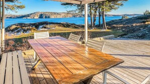 A wooden deck with a table and chairs, overlooking a coastal landscape with cliffs and a body of water. - Beautiful home in Lysekil (Lysekil)