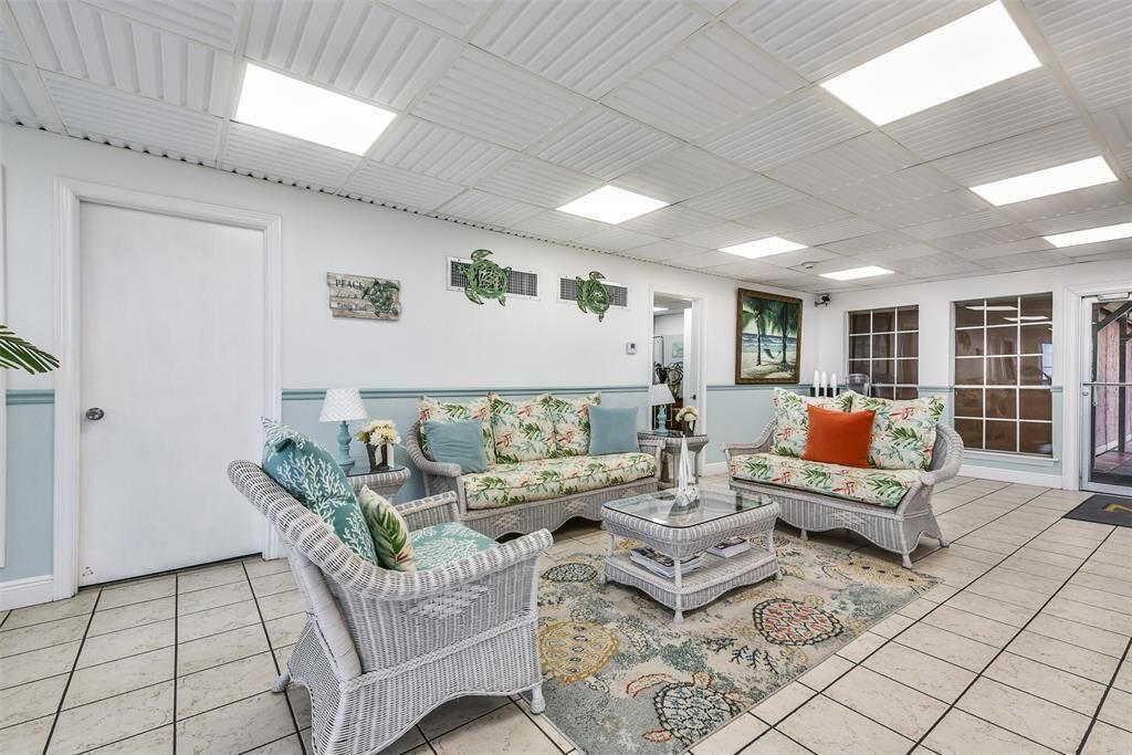 A spacious living room with wicker furniture, a patterned rug, and a view of the outdoors through large windows.