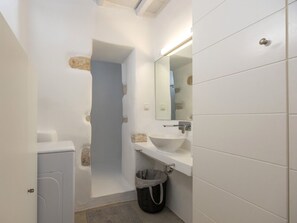 A bathroom with a white sink, mirror, and towel rack. There is a trash bin and a door leading to another room. - Walkable distance from everything you need (Paros)
