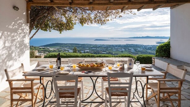 An outdoor dining area with a table set for two, overlooking a scenic view of the sea and landscape. - Alepou House - Gorgeous scenery (Aliki)