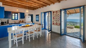 A modern kitchen with blue cabinets, a wooden ceiling, and a dining area with white chairs. - Alepou House - Gorgeous scenery (Aliki)
