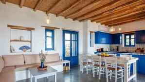 A modern living room with a sofa, coffee table, and dining area with chairs. There is a kitchen with blue cabinets and a wooden ceiling. - Alepou House - Gorgeous scenery (Aliki)