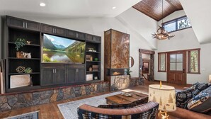 A spacious living room with a stone fireplace, a large flat-screen TV, and a cozy seating area with a patterned rug and a wooden coffee table. - 34 Acre Escape~Games~Hiking~Pool Table~Bicycles (Black Hawk)