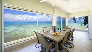 Un comedor con una mesa grande, sillas y vista al océano a través de amplios ventanales.