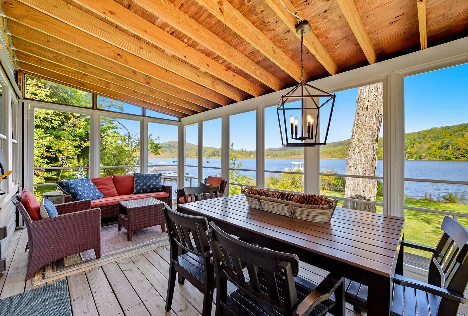 Ein überdachter Außenbereich mit Holztisch und Stühlen, mit Blick auf einen See.