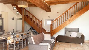 A spacious living area with a high wooden ceiling, a staircase, a dining table set with chairs, and a sofa. - Comfortable cottage, 2 bedrooms, garden, near Blois & Chambord (Saint-Claude-de-Diray)