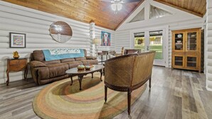 A log cabin interior with a brown leather sofa, wicker chair, and a round coffee table. - Farm Experience in a Beautiful Log Cabin (LaFayette)