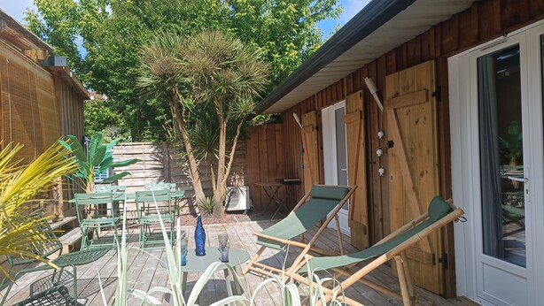 Une terrasse en bois avec des meubles d’extérieur, un arbre et une porte-fenêtre coulissante.