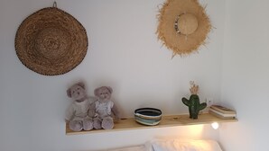 Une pièce avec un mur blanc, deux chapeaux en fibres tressées, une étagère avec un cactus, un ours en peluche et un bol.