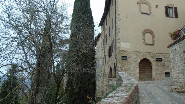Un bâtiment en pierre doté d’une grande porte en arc de cercle, d’un étroit sentier pavé et de grands arbres.